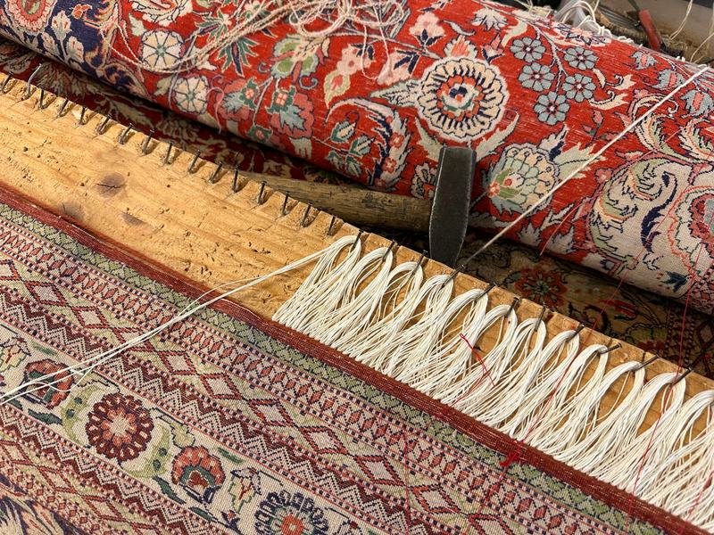Tapis persan rouge tendu sur l’établi de l’atelier pendant la pose de franges neuves