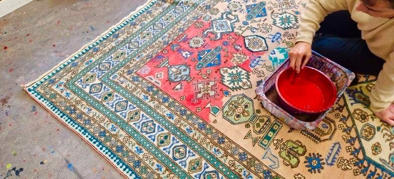 Application d’une teinture naturelle rouge au pinceau sur un tapis clair, au sol de l’atelier