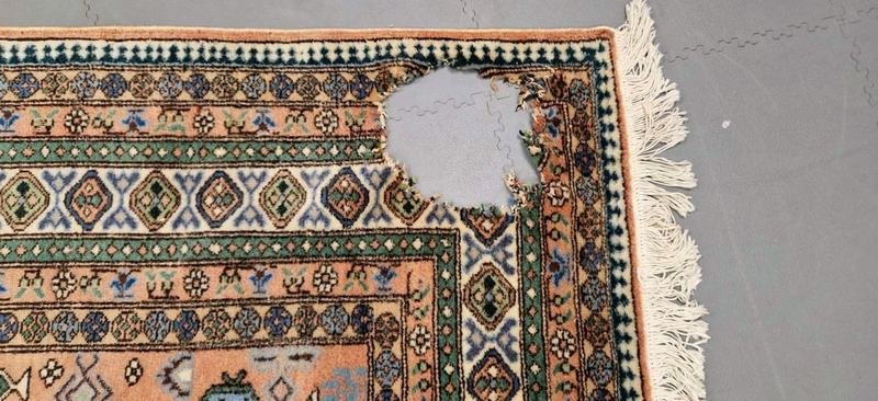 Trou net dans le champ d’un tapis clair à franges, avant retissage